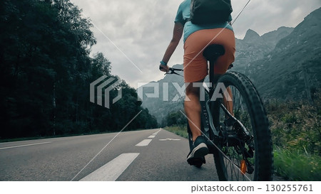 Rear view of a cyclist riding on a road in the French Alps, camera following behind the rider. Scenic mountain landscape Rear view of a cyclist riding on a road in the French Alps, camera following behind the rider. Scenic mountain landscape 130255761