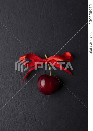 One juicy ripe fresh cherry with a red bow on a black background. Seasonal fruits, harvest. Selective focus, close-up. 130256036