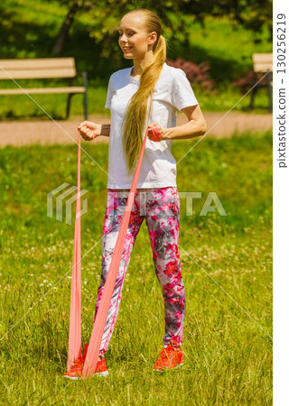 Girl doing exercises outdoor, using resistance fit band. 130256219