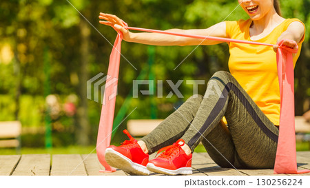 Girl doing exercise outdoor, using resistance fit band. 130256224
