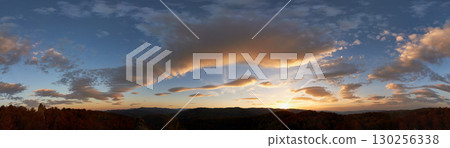 Stunning sunset fills sky with rich hues of blue and orange. Dramatic clouds with hints of pink and gold spread across sky. Silhouettes of hills in foreground add depth to breathtaking evening scene. 130256338