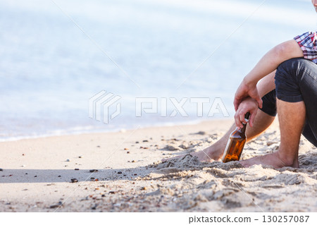Man depressed with wine bottle sitting on beach outdoor Man depressed with wine bottle sitting on beach outdoor 130257087