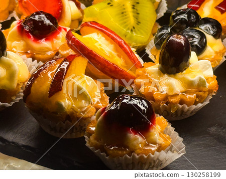Close-up of fruit tartlets with cream and berries. Sweet colorful pastries, gourmet patisserie and festive indulgence. 130258199
