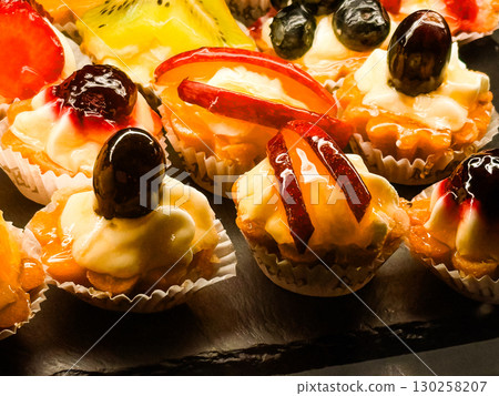Mini fruit tarts with cream and fresh berries. Colorful confectionery, sweet dessert and gourmet patisserie display. 130258207