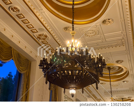 Ornate chandelier and golden ceiling in luxury hotel. Classic architecture, intricate details and elegant evening interior. Ornate chandelier and golden ceiling in luxury hotel. Classic architecture, intricate details and elegant evening interior. 130258208