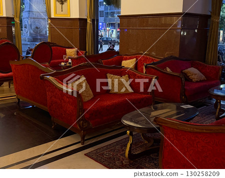 Multiple red vintage sofas in hotel lounge interior. Classic decor with glass tables, ornate details and evening atmosphere. 130258209