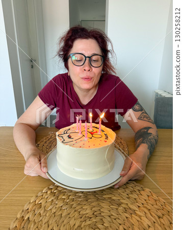 Woman blowing out candles on birthday cake. Celebration, tradition and joyful wish-making moment at festive party. 130258212
