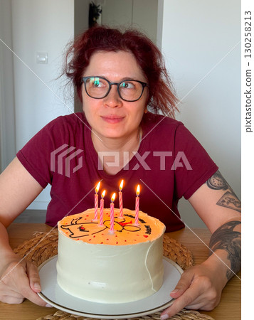 Happy woman holding birthday cake with lit candles. Celebration, joy and festive atmosphere at home gathering. Happy woman holding birthday cake with lit candles. Celebration, joy and festive atmosphere at home gathering. 130258213