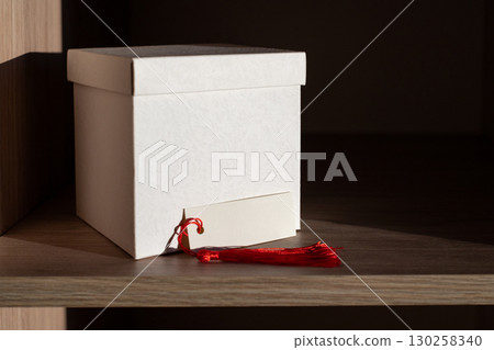 White Box and Blank card with Red Tassel Displayed on Wooden Shelf White Box and Blank card with Red Tassel Displayed on Wooden Shelf 130258340