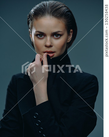 serious woman with short wet hair wearing black turtleneck posing with hand near face 130258438