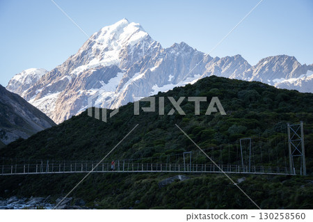 Tourist walking a swing bridge with huge snowy mountain in backdrop, Mt Cook, New Zealand Tourist walking a swing bridge with huge snowy mountain in backdrop, Mt Cook, New Zealand 130258560