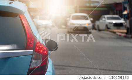 Close up of a blue car tail light in heavy traffic. The sun lens flare and blurred background of other vehicles highlight the frustration of a traffic jam during a daily urban commute. Close up of a blue car tail light in heavy traffic. The sun lens flare and blurred background of other vehicles highlight the frustration of a traffic jam during a daily urban commute. 130259183