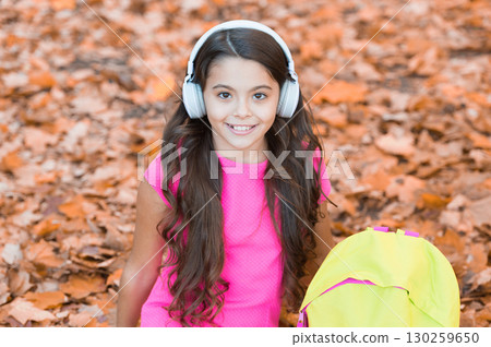 Happy childhood. kid listen music in autumn park. fall is a time for study. back to school. concept of online education. child sit in autumn leaves. girl in earphones with school bag Happy childhood. kid listen music in autumn park. fall is a time for study. back to school. concept of online education. child sit in autumn leaves. girl in earphones with school bag 130259650