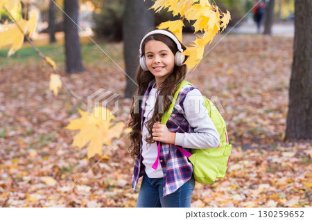 kid in autumn park. happy kid walk among autumn leaves. small girl wear headphones. back to school. modern education. child with school backpack in fall forest. concept of knowledge day kid in autumn park. happy kid walk among autumn leaves. small girl wear headphones. back to school. modern education. child with school backpack in fall forest. concept of knowledge day 130259652