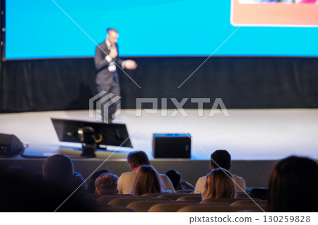 Presenter at business conference delivering speech to audience with digital screen 130259828