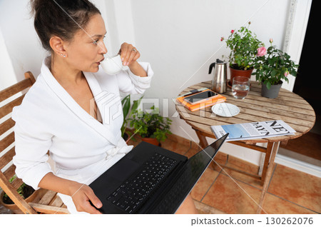 Woman Relaxing Outdoors While Working on Laptop and Enjoying Coffee Woman Relaxing Outdoors While Working on Laptop and Enjoying Coffee 130262076