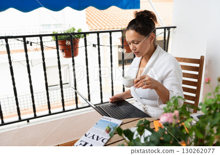 Woman Working on a Laptop While Drinking Coffee on a Balcony 130262077