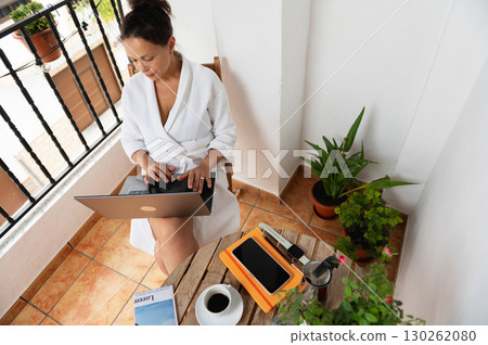 Woman Working From a Balcony on a Laptop Surrounded by Plants 130262080