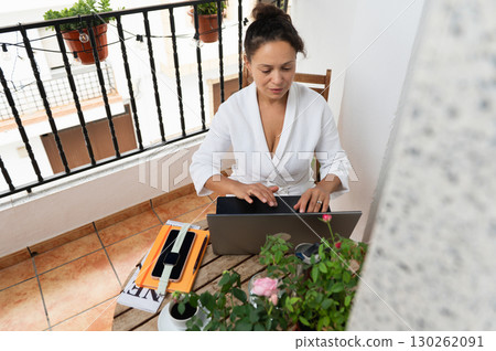 Woman Working on Laptop at Cozy Balcony Table with Plants and Accessories Woman Working on Laptop at Cozy Balcony Table with Plants and Accessories 130262091