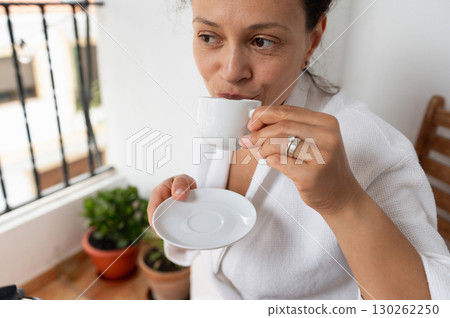 Woman Enjoying Relaxing Moment With Coffee on a Sunlit Balcony 130262250
