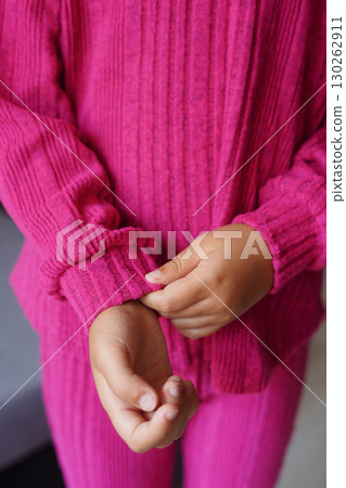 A close-up of a child wearing a vibrant pink ribbed knit outfit with hands adjusting the sleeve 130262911
