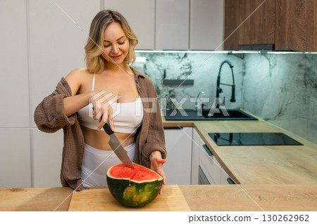 A sensual woman enjoys a slice of juicy watermelon in a modern kitchen. Confident, playful, and radiant, she savors the moment with a hint of summer flirtation. A sensual woman enjoys a slice of juicy watermelon in a modern kitchen. Confident, playful, and radiant, she savors the moment with a hint of summer flirtation. 130262962
