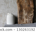 Minimalist still life with a white ceramic vase holding dry branches, placed against a rustic wooden board and textured concrete wall. Natural wabi-sabi style composition. 130263192