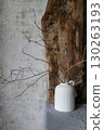 Minimalist still life with a white ceramic vase holding dry branches, placed against a rustic wooden board and textured concrete wall. Natural wabi-sabi style composition. 130263193