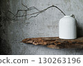 Minimalist still life with a white ceramic vase holding dry branches, placed against a rustic wooden board and textured concrete wall. Natural wabi-sabi style composition. 130263196