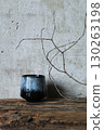 Minimalist still life with a dark ceramic vase and dry branch on rustic wood against a textured concrete wall. Wabi-sabi style composition 130263198