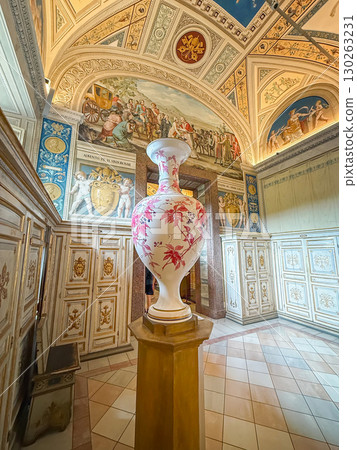 VATICAN CITY, ROME, ITALY - AUGUST 02, 2025 Elegant white porcelain vase with red floral motifs, standing on a wooden pedestal in a richly decorated museum room with painted vaulted ceilings 130263231