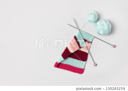 Brown beige vinous and turquoise piece of striped knitting with knitting needles and balls of thread on gray background. Homemade needlework and knitting of warm, clothes and toys. Concept creativity Brown beige vinous and turquoise piece of striped knitting with knitting needles and balls of thread on gray background. Homemade needlework and knitting of warm, clothes and toys. Concept creativity 130263259