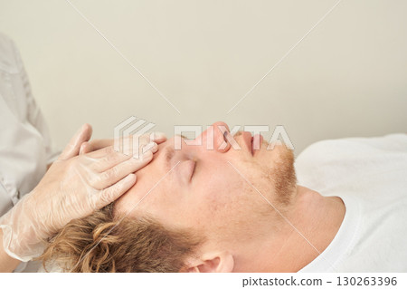 Young caucasian male receiving facial treatment with gentle hand massage 130263396
