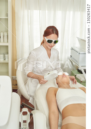 Young caucasian female receiving laser facial treatment in modern aesthetic 130263417