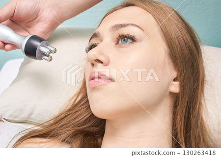 Relaxed female receiving facial treatment with advanced beauty device in spa 130263418