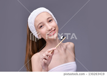 Young caucasian female holding bamboo toothbrush with charcoal toothpaste in spa 130263419