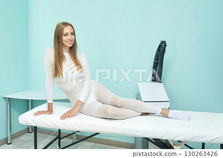 Smiling caucasian female in white bodysuit relaxing on massage table in modern 130263426