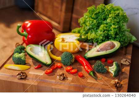 Colorful fresh vegetables and avocado on a wooden board in cozy kitchen setting Colorful fresh vegetables and avocado on a wooden board in cozy kitchen setting 130264040
