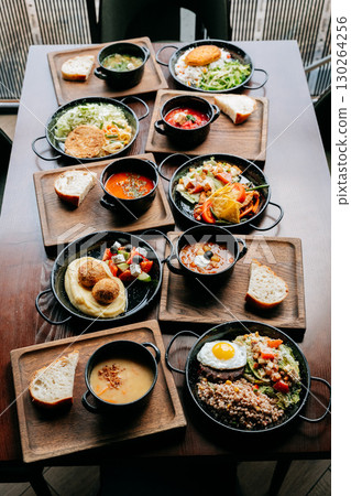 Assorted restaurant-style meals served in black bowls on wooden trays, top view 130264256