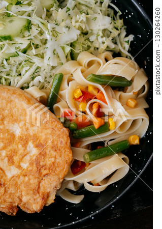 Closeup of fried cutlet with pasta, vegetables, and fresh cabbage cucumber salad 130264260