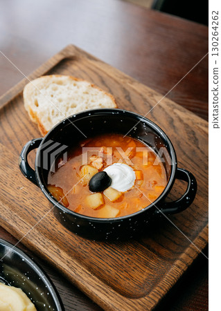Hot bowl of rustic solyanka soup with sour cream, black olive, and fresh bread slice 130264262