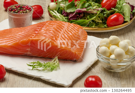Raw salmon fillet with mozzarella cheese, cherry tomato and fresh salad on wooden table Raw salmon fillet with mozzarella cheese, cherry tomato and fresh salad on wooden table 130264495