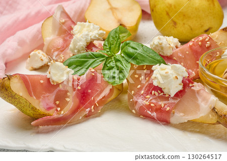 Pear slice wrapped in prosciutto with cheese and sesame seeds on a white board Pear slice wrapped in prosciutto with cheese and sesame seeds on a white board 130264517
