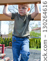 A child climbs up an alpine grid in a park on a playground on a hot summer day. children's playground in a public park, entertainment and recreation for children, mountaineering training. High quality 130264616