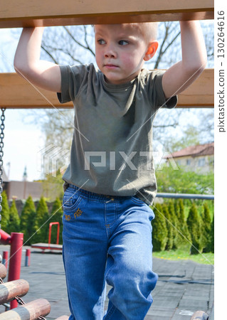 A child climbs up an alpine grid in a park on a playground on a hot summer day. children's playground in a public park, entertainment and recreation for children, mountaineering training. High quality 130264616