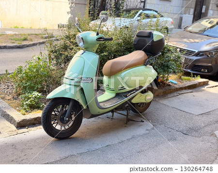 Mint green retro scooter with beige seat parked on city street near sidewalk. Urban mobility, eco transport, and stylish modern lifestyle 130264748