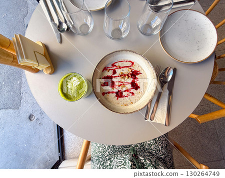 Top view of oatmeal porridge with raspberry topping and matcha latte on round cafe table. Healthy breakfast, modern nutrition, and wellness dining lifestyle 130264749