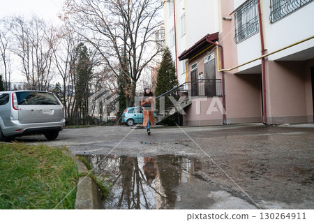 Woman walking through a parking lot after rain, reflecting puddles along the path in a quiet neighborhood setting during early evening hours 130264911