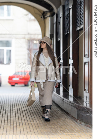 Stylish woman explores urban alleyway while showcasing contemporary fashion on a chilly day in a vibrant city environment 130264918
