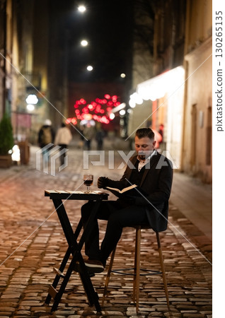 Charming evening in a bustling street with a reader enjoying a glass of wine, surrounded by twinkling lights and lively activity in a cozy ambiance Charming evening in a bustling street with a reader enjoying a glass of wine, surrounded by twinkling lights and lively activity in a cozy ambiance 130265135